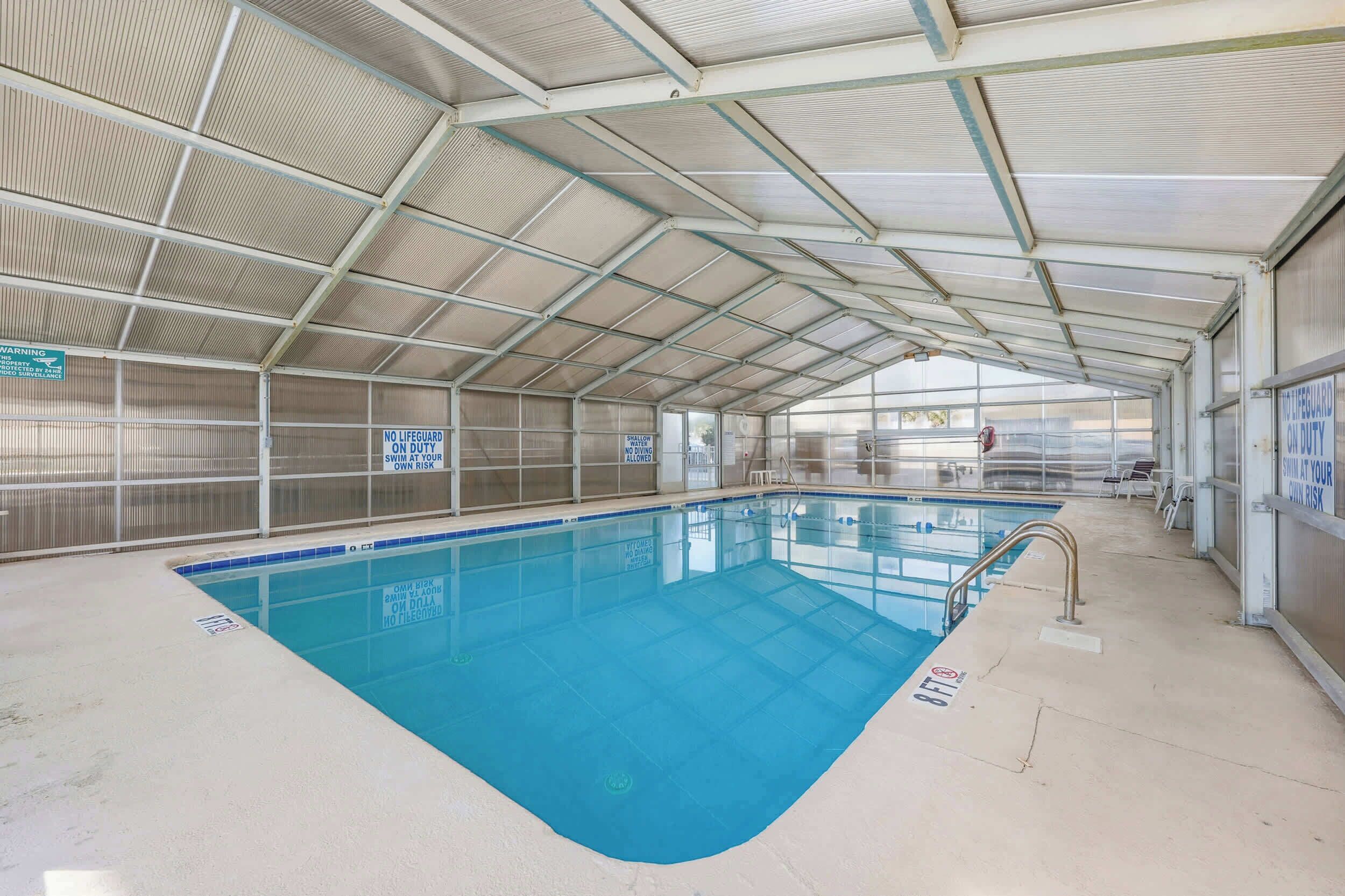 Une piscine intérieure dotée d’un toit couvert, d’une signalisation claire et d’un sol carrelé.