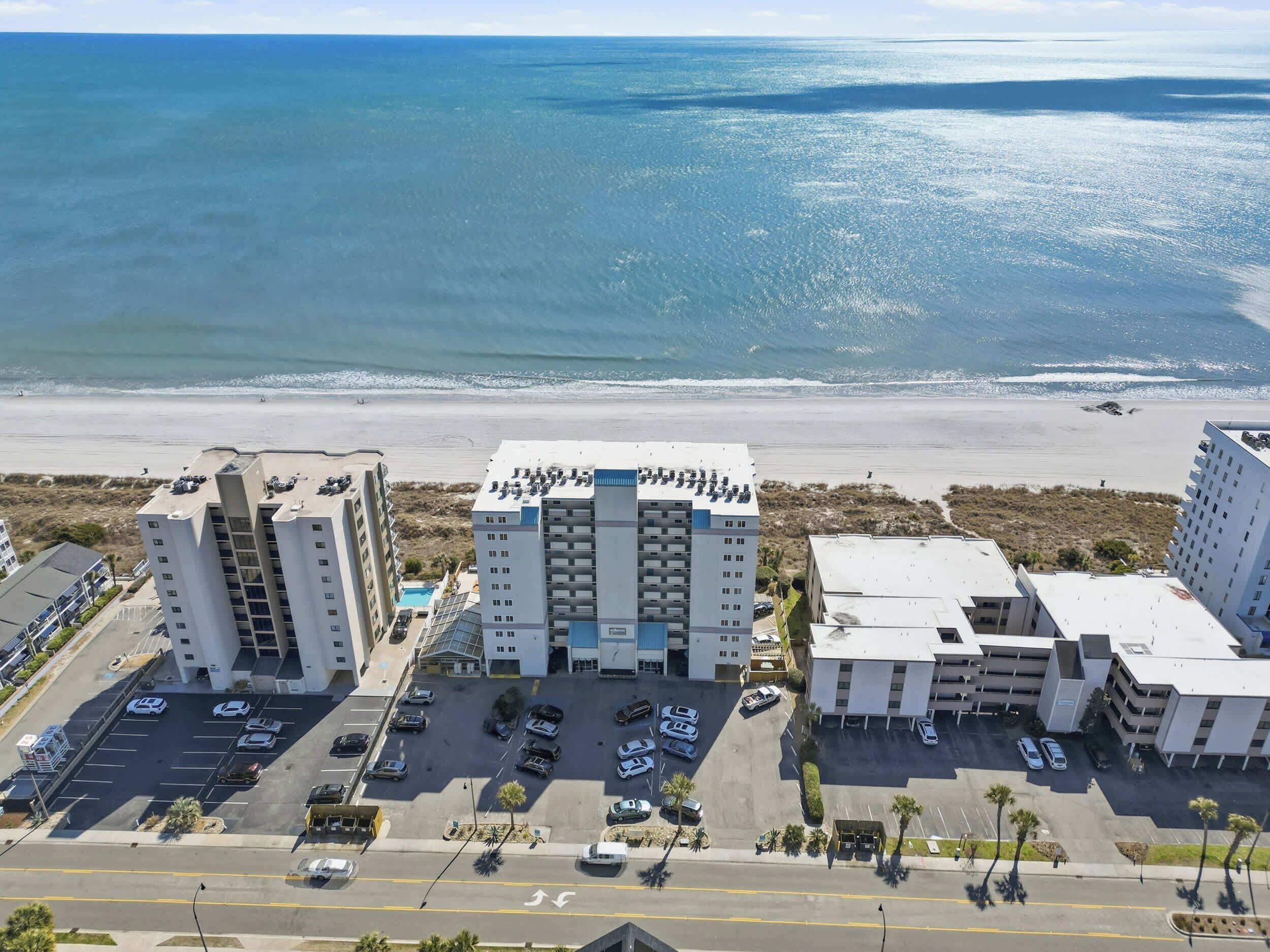 A beachfront hotel with multiple buildings, a parking lot, and a view of the ocean.