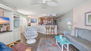 Una sala moderna con sofá, sillón y comedor, con una cocina al fondo.