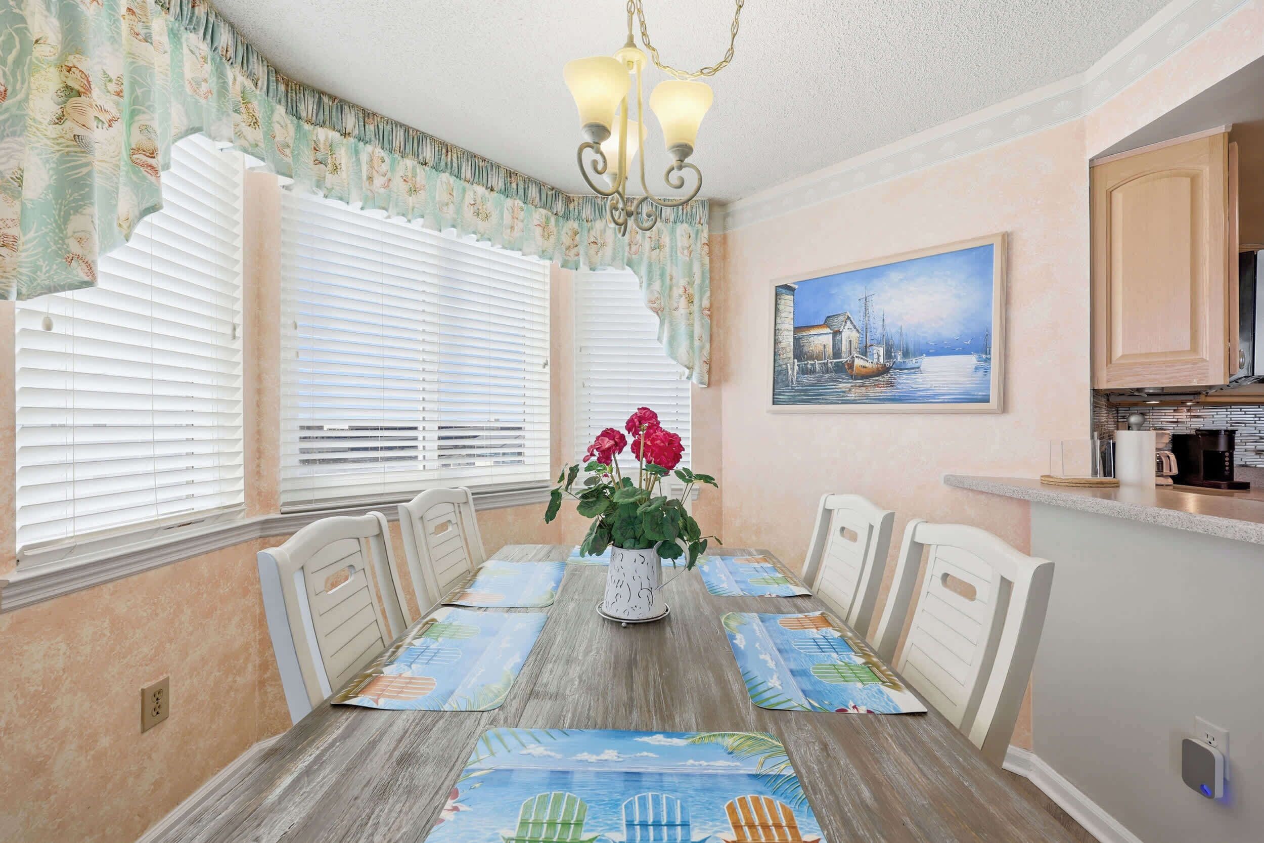 A dining area with a wooden table, white chairs, a vase with flowers, and a painting on the wall.
