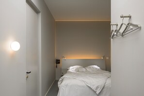 A minimalist hotel room with a bed, bedside table, and a wall-mounted coat rack. - Hôtel Continental (Saint-Etienne)