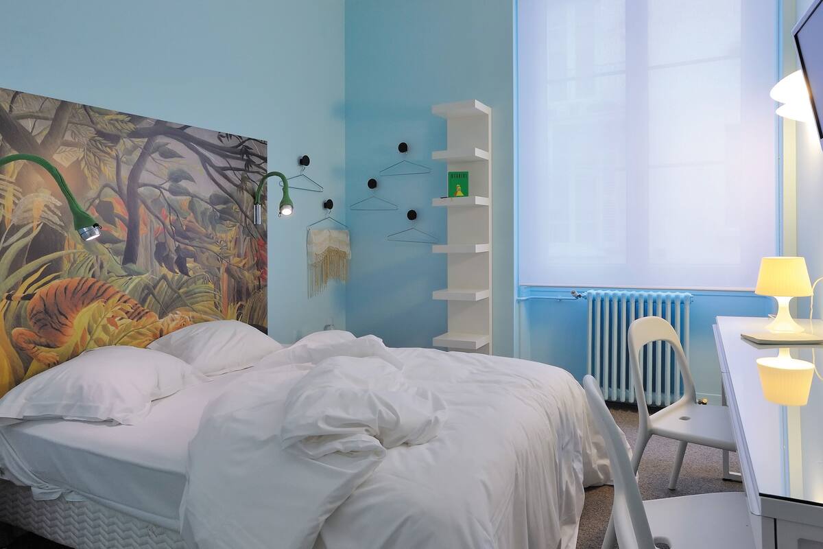 Un dormitorio con cama, escritorio, silla, radiador y un cuadro en la pared.