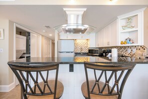 Een moderne keuken met een centraal eiland, twee barkrukken, een magnetron en een decoratieve wand.