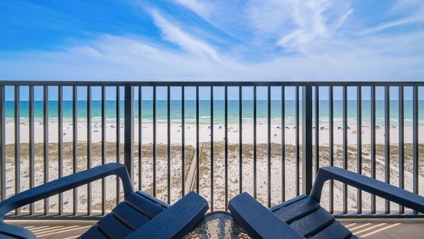 Une vue sur la plage depuis un balcon doté d’une balustrade, avec des chaises de plage et un ciel dégagé.