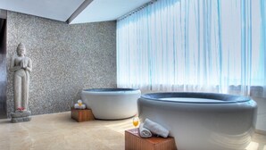 Ett modernt spa-rum med en staty, två bubbelbad och ett stort fönster med gardiner.