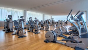 Ett rymligt gym med olika konditionsmaskiner, styrketräningsstationer och ett stort fönster som släpper in naturligt ljus.