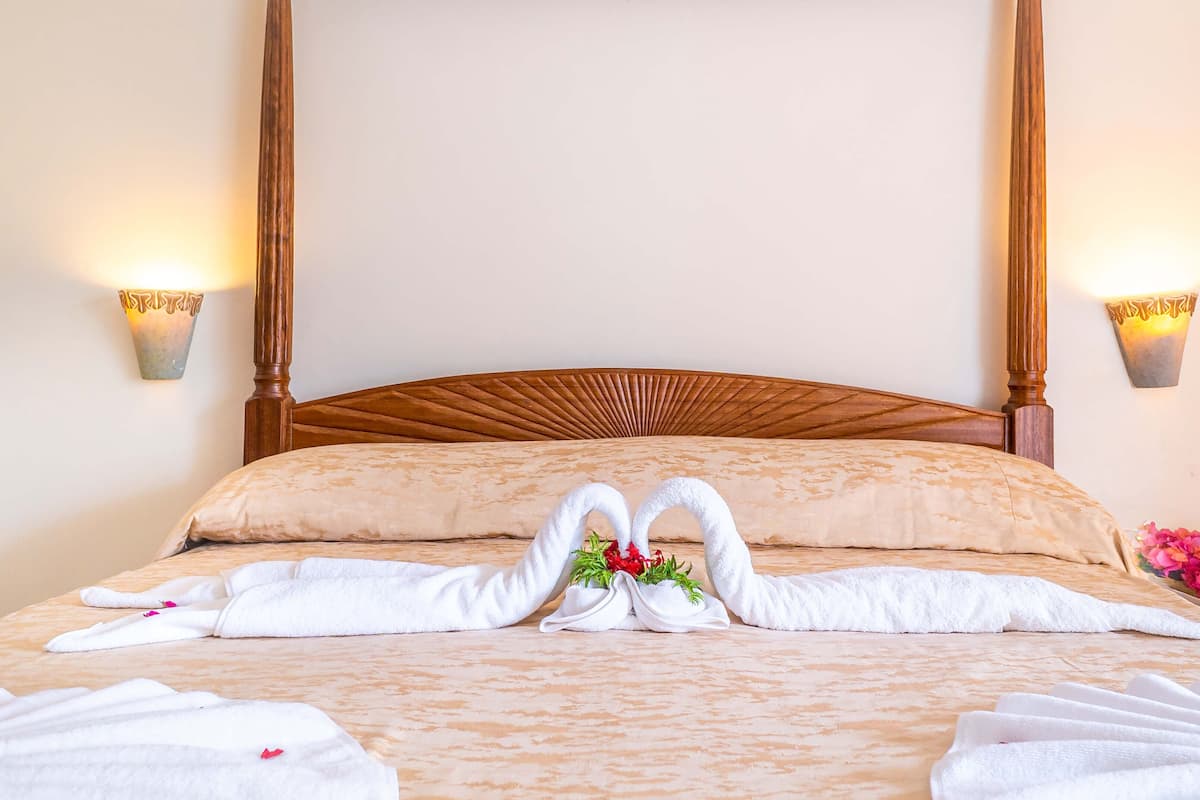 A neatly made bed with two towels arranged in a heart shape, a wooden headboard, and two wall-mounted lamps.