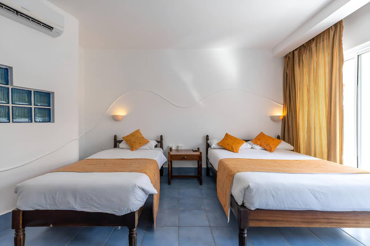 A hotel room with two beds, a small table, and a wall-mounted air conditioner.