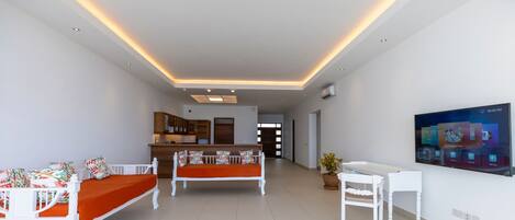 A modern living room with a sofa, a dining table, and a TV mounted on the wall.