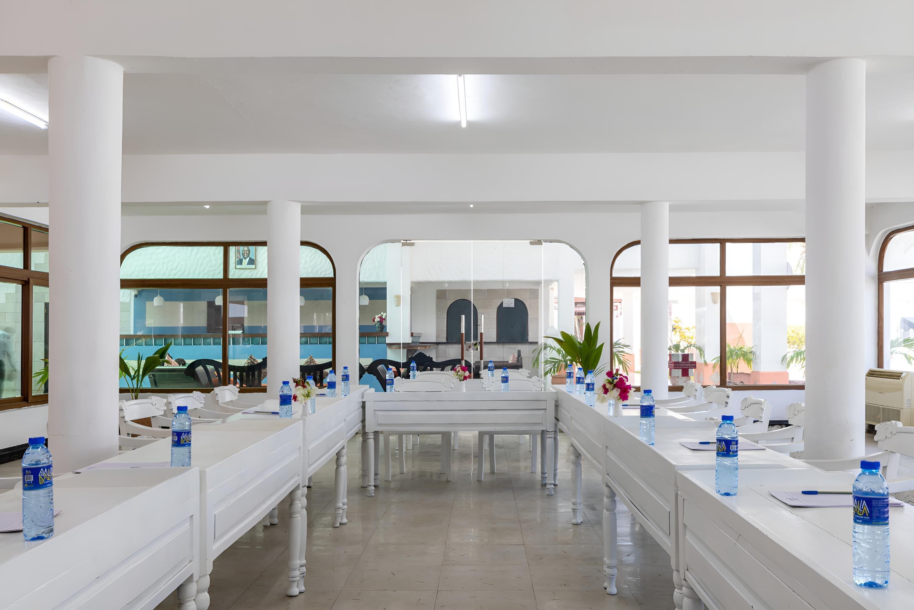 A spacious conference room with white tables, chairs, and water bottles.