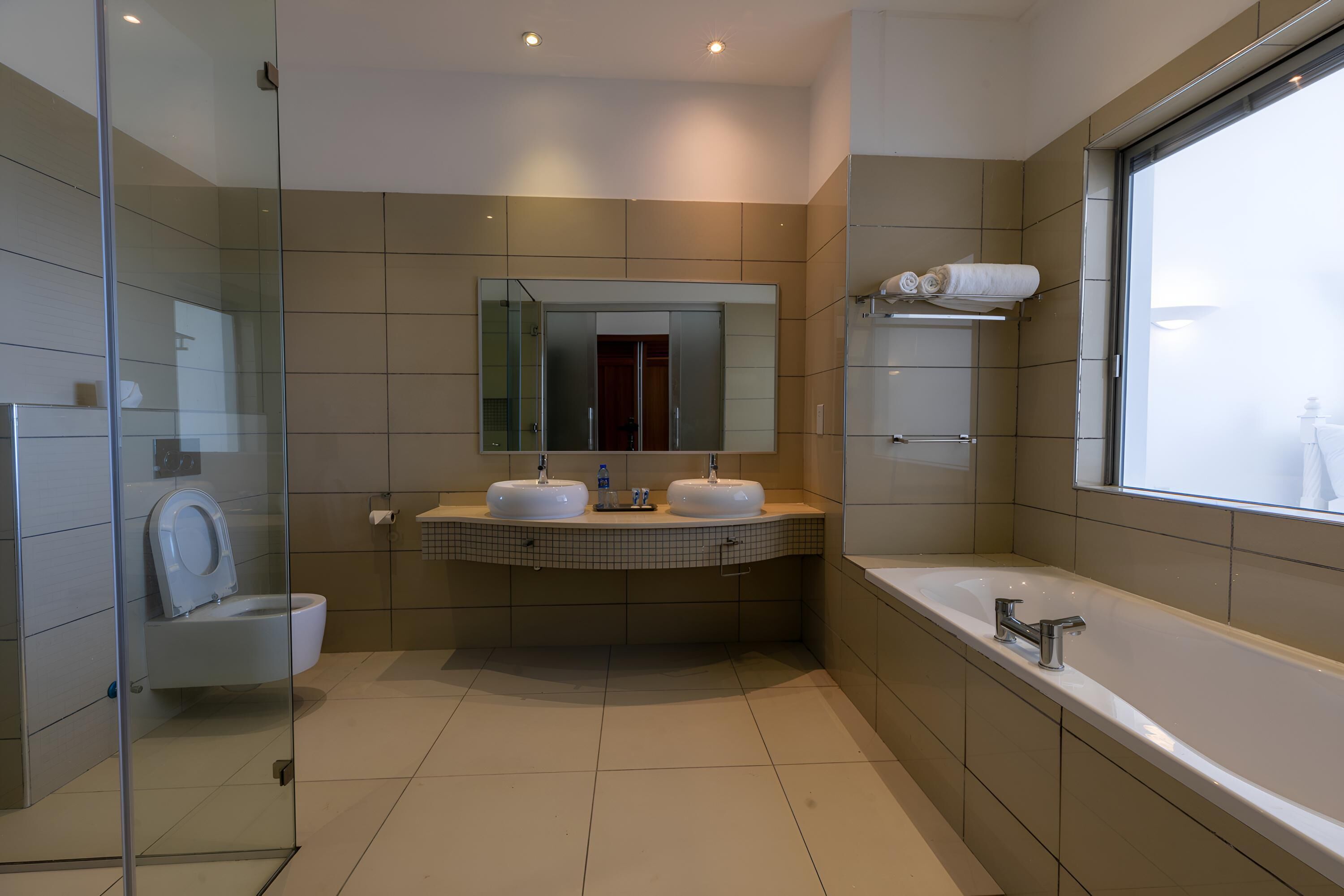 Un baño moderno con dos lavamanos, una ducha con cerramiento de vidrio y una bañera amplia.