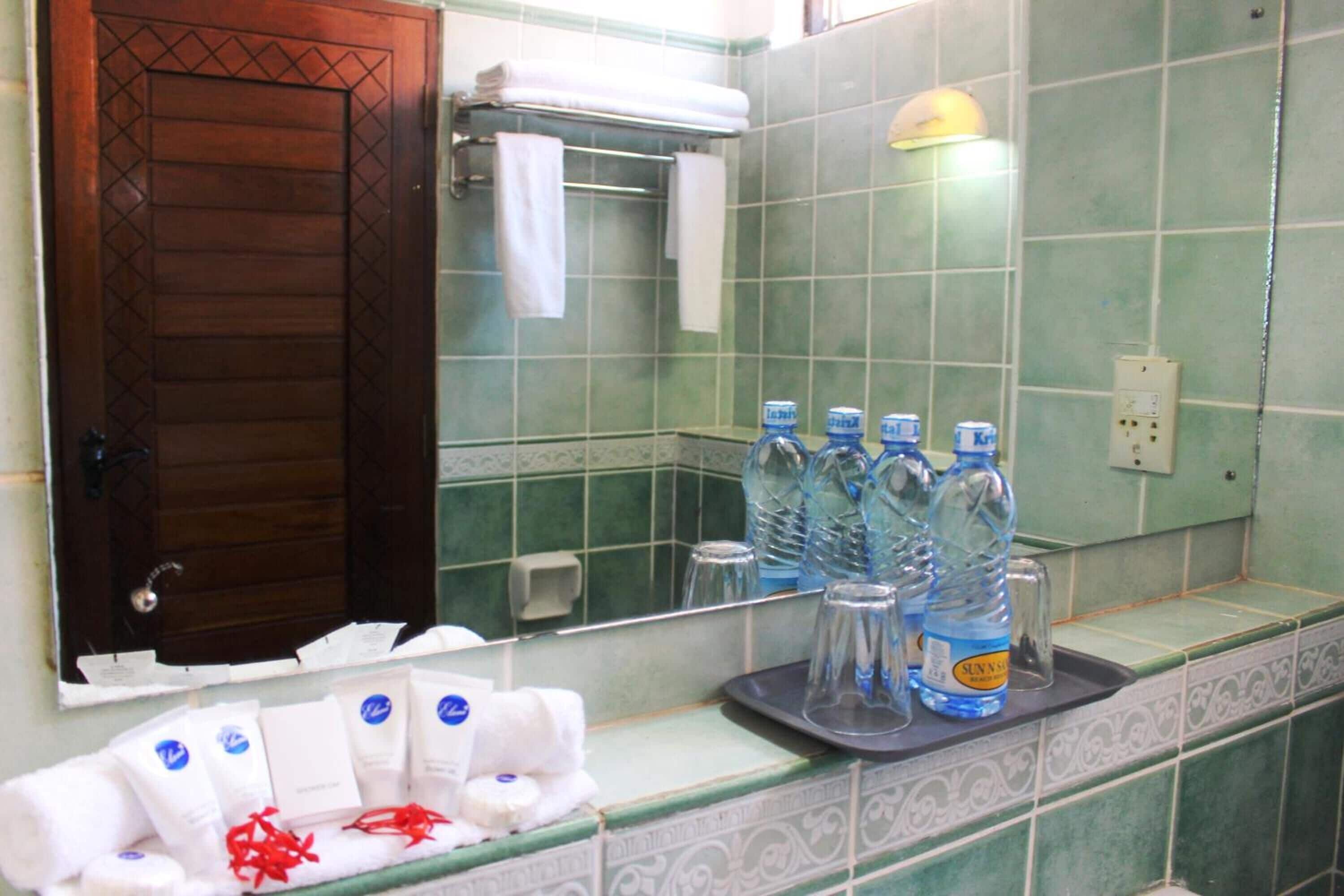A bathroom with green tiles, a wooden door, and toiletries on the counter.