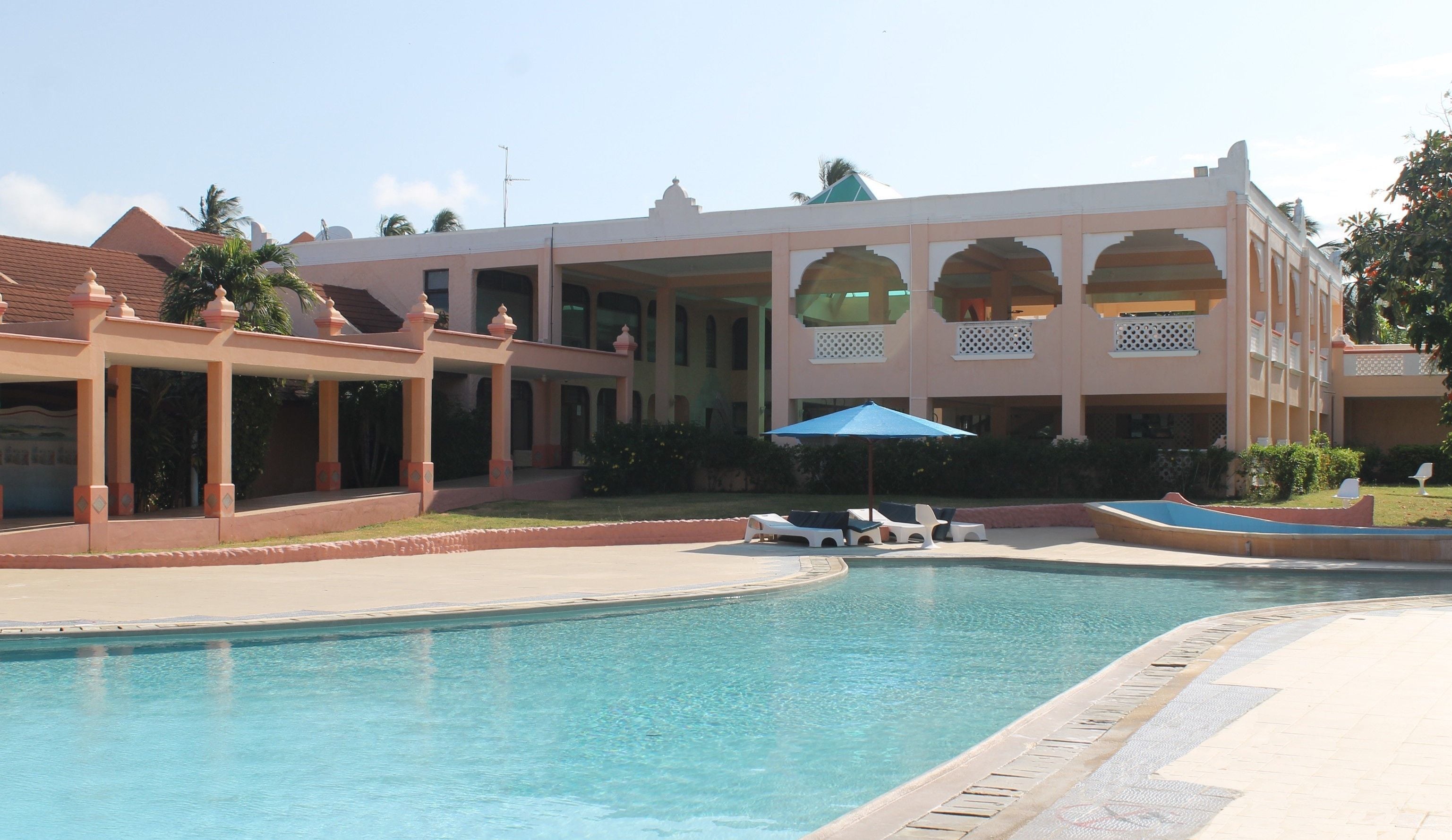 A hotel with a swimming pool, covered outdoor seating, and a large building with multiple balconies.