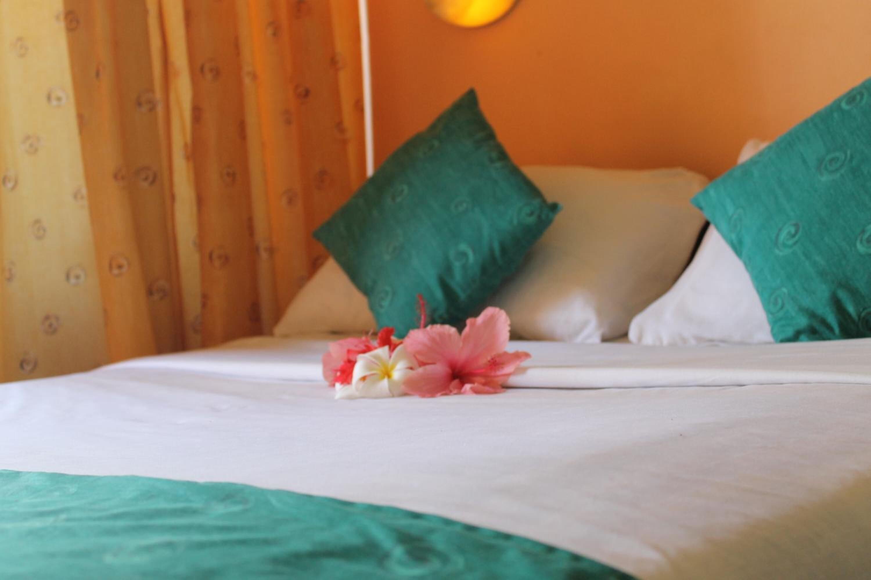 Un lit avec une literie blanche, des oreillers verts et un arrangement floral.