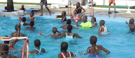 Une zone autour d’une piscine, avec des personnes dans l’eau et un but de football protégé par un filet.