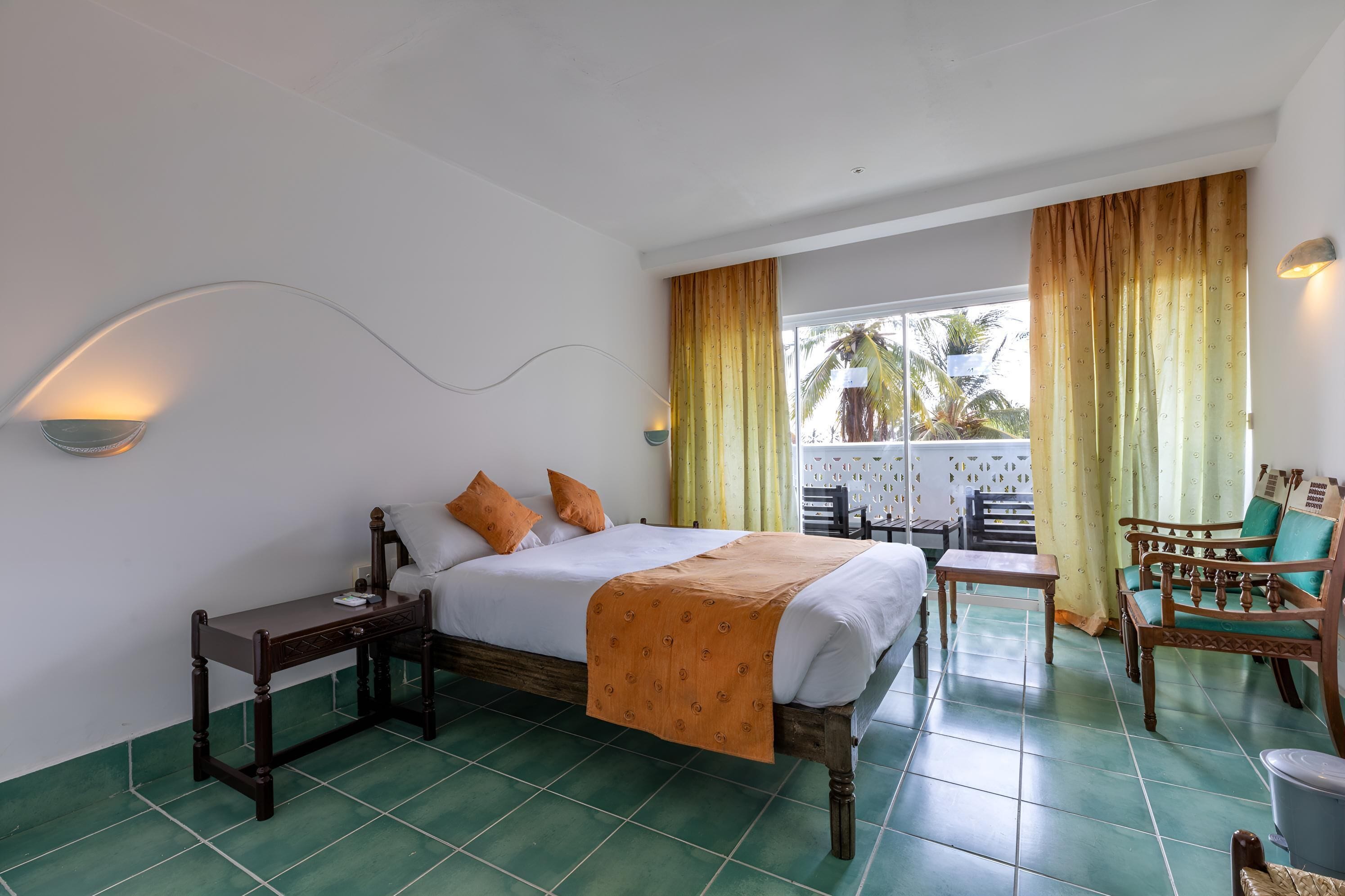 Habitación de hotel con cama, mesita de noche, silla y vistas al exterior.
