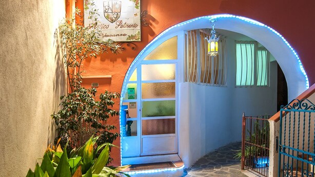 Una entrada arqueada con un letrero de azulejos, un patio empedrado de piedra y un arco iluminado en azul.