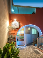 Una entrada arqueada con un letrero de azulejos, un patio empedrado de piedra y un arco iluminado en azul.