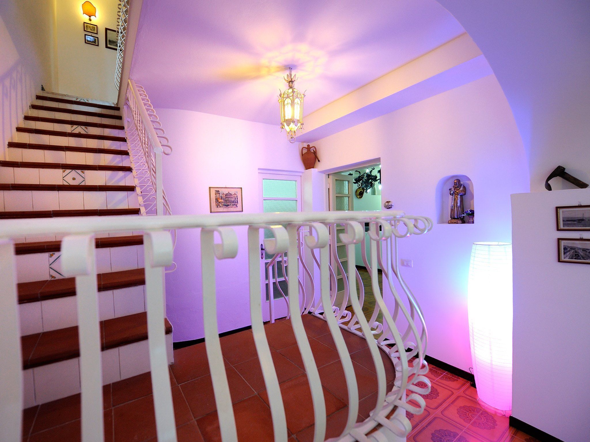 A staircase with white railings and wooden steps, leading to a landing with a chandelier and wall-mounted decorations.