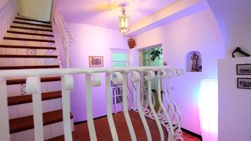 A staircase with white railings and wooden steps, leading to a landing with a chandelier and wall-mounted decorations.