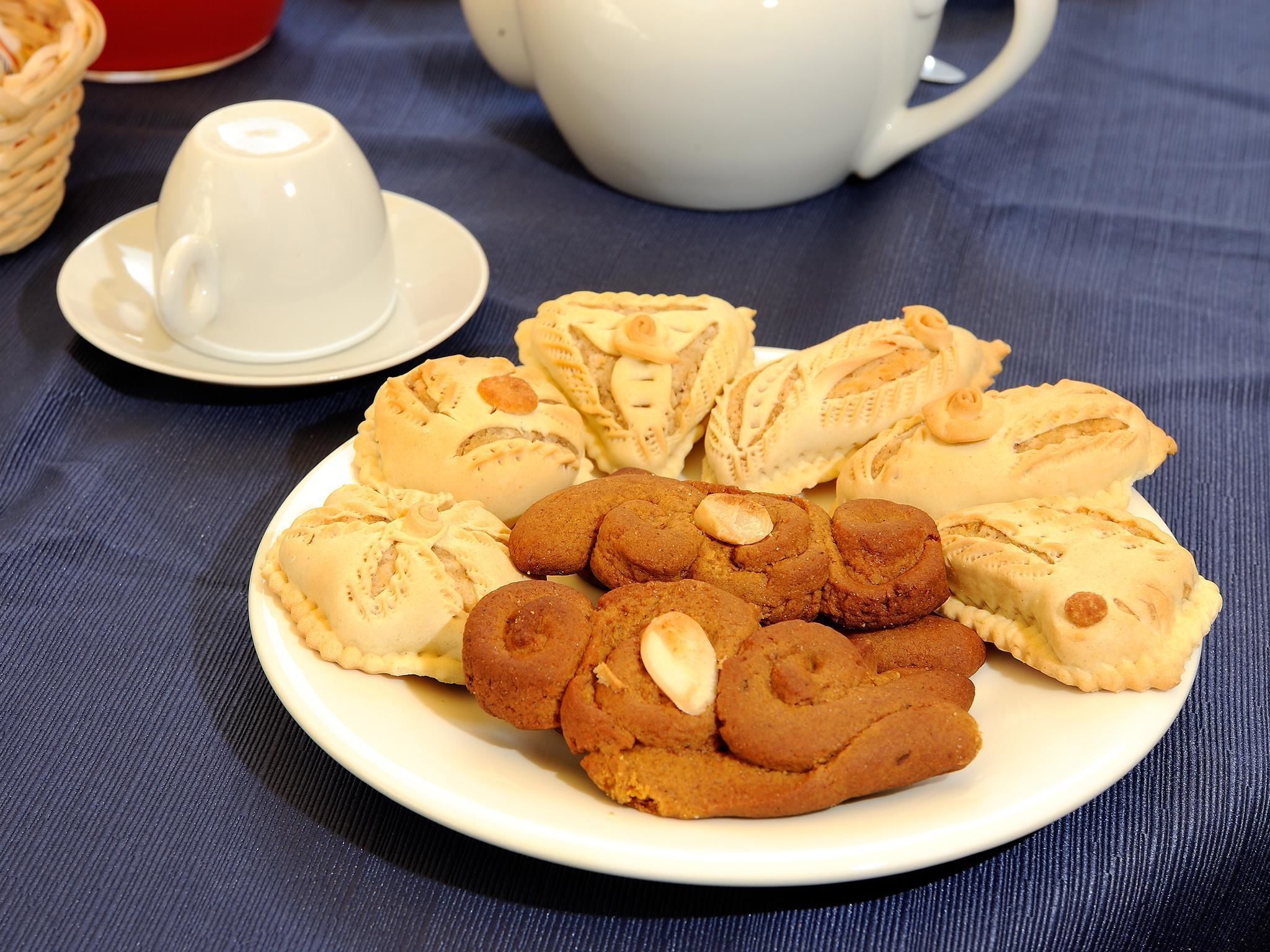A plate of cookies and pastries on a table with a teapot and cups in the background.