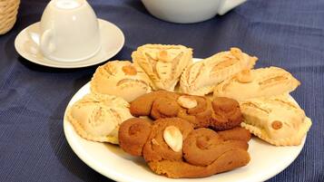 A plate of cookies and pastries on a table with a teapot and cups in the background.