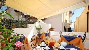 Un área de comedor al aire libre con mesas dispuestas para el desayuno, mostrando platos de pasteles y una jarra de jugo.