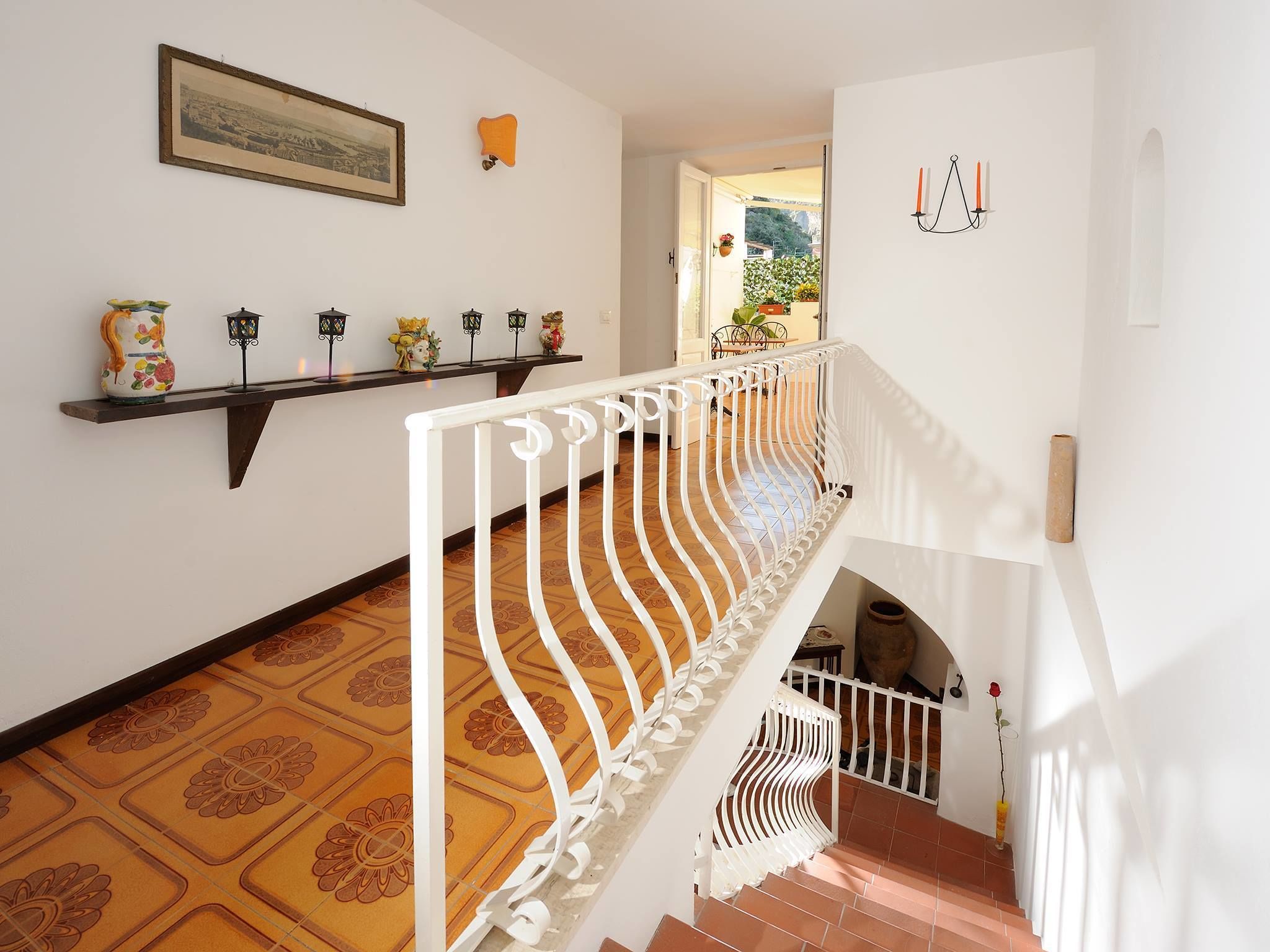 Una escalera con barandilla blanca, suelo estampado, un estante con adornos y un cuadro en la pared.