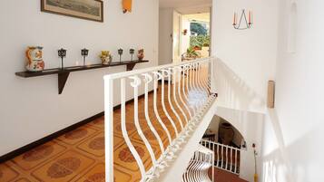 Una escalera con barandilla blanca, suelo estampado, un estante con adornos y un cuadro en la pared.
