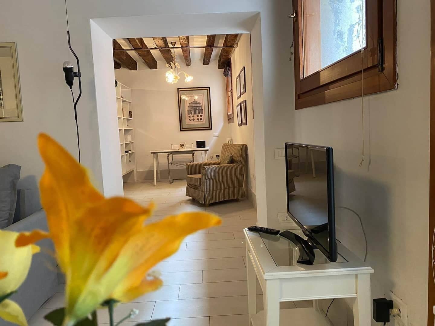Una sala de estar con televisión sobre un mueble bajo, una estantería, un sillón a rayas y una mesa de comedor con sillas.