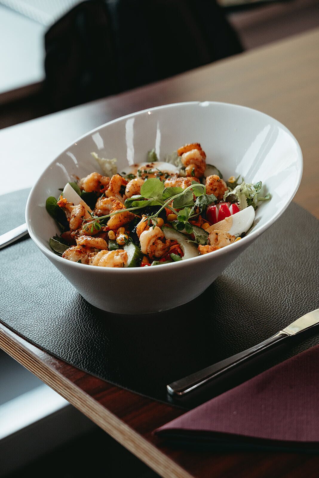 A bowl of food on a table with a napkin and a knife.