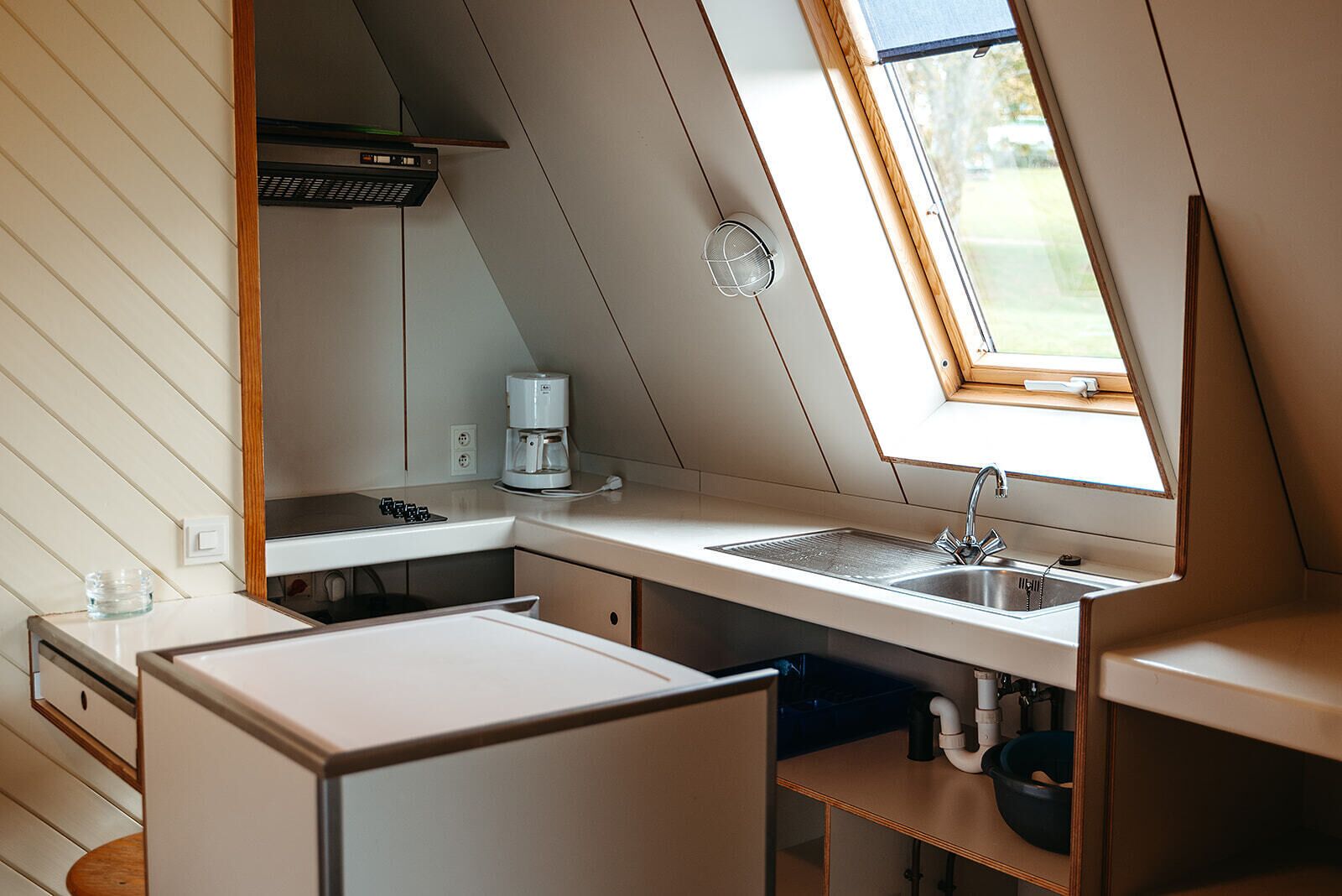 Een kleine keuken met een raam, een koffiezetapparaat en een spoelbak.