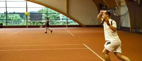 An indoor tennis court with a high ceiling and large windows.