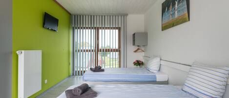 Habitación de hotel con dos camas, un televisor, un cuadro y una ventana con persianas.
