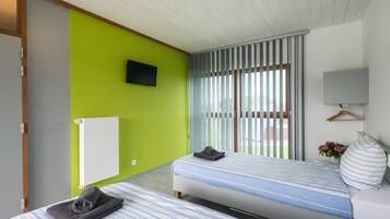 A bedroom with two beds, a green wall, a TV, and a window with blinds.