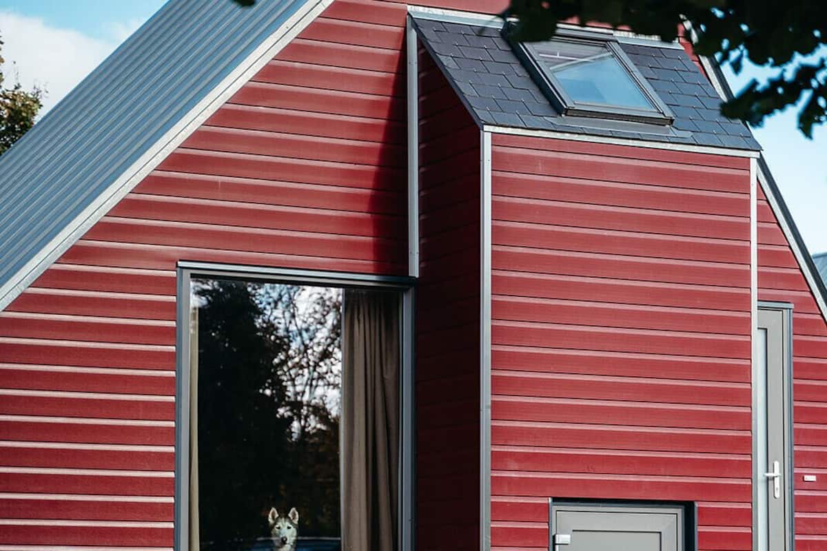 A red building with a large window and a door, a picnic table in front, and a grassy area with fallen leaves.
