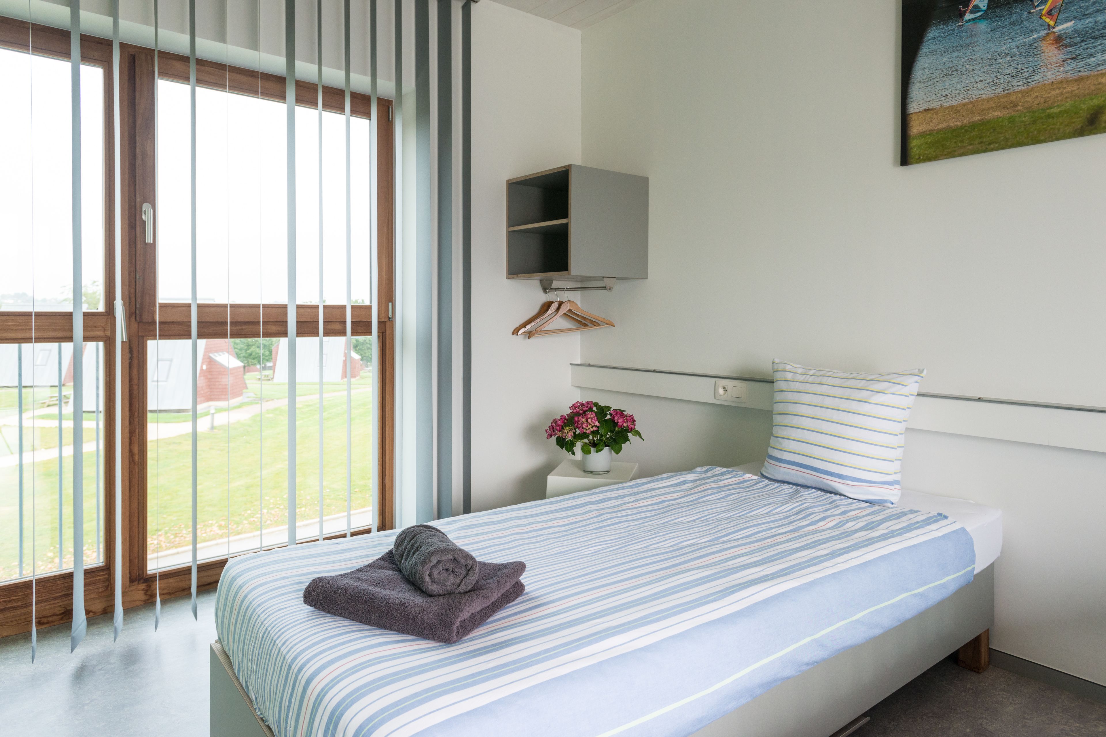 Un dormitorio con cama, una planta colgante y un cuadro en la pared.