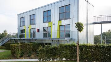 Un edificio moderno con múltiples ventanas y puertas, una escalera y un seto bien cuidado al frente.