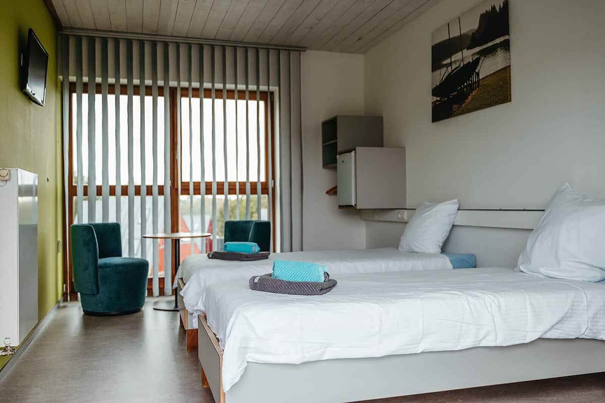 A hotel room with two beds, a chair, a table, and a painting on the wall.
