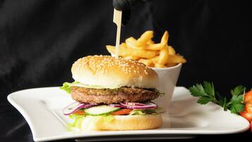 Een hamburger met sesamzaadbolletje, sla, tomaat en rode ui, geserveerd met frietjes op een wit bord.
