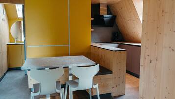 Een kleine keuken met een houten aanrecht, twee witte stoelen en een gele accentmuur.