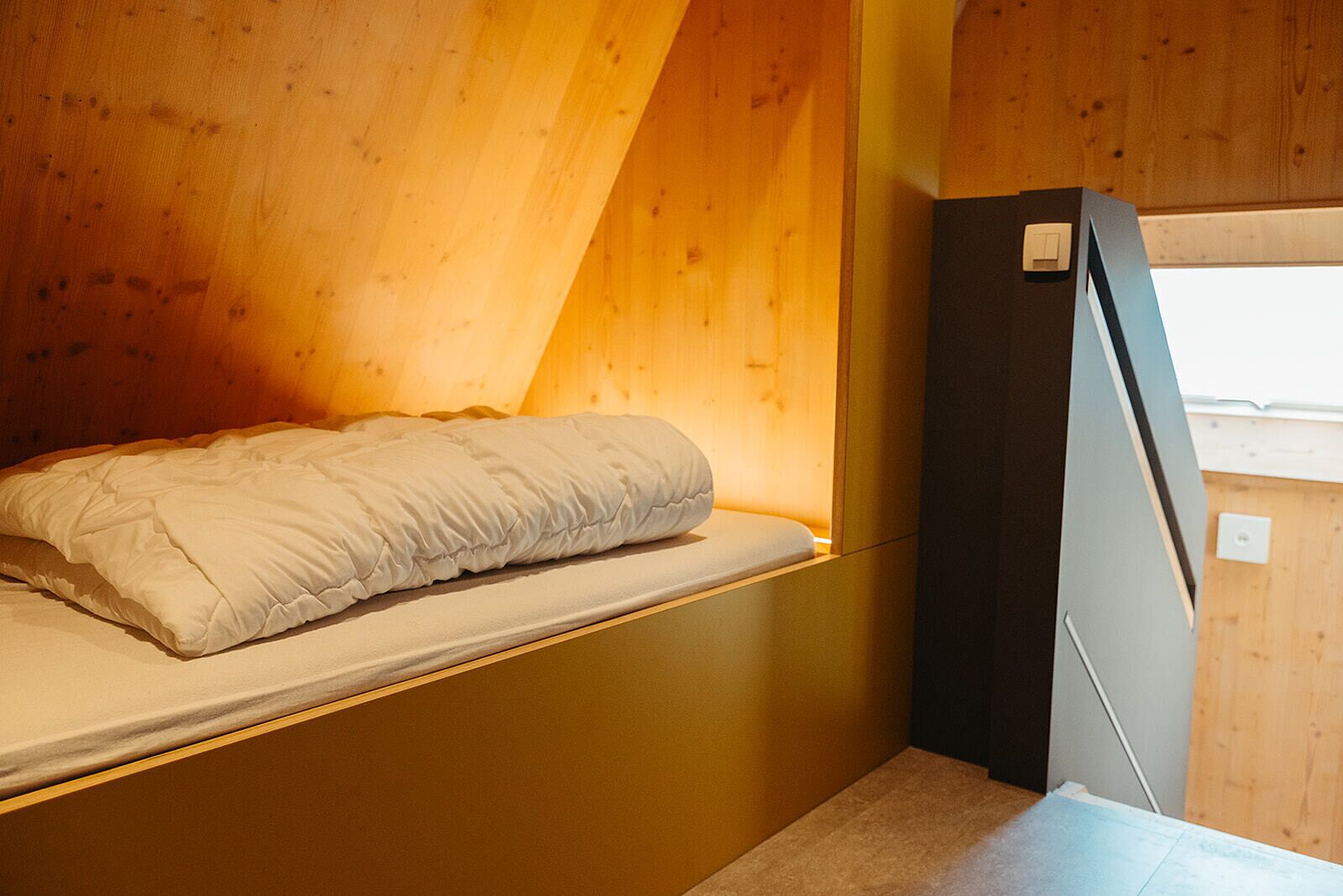 Ein kleines Zimmer mit Bett, Fenster und Kühlschrank.