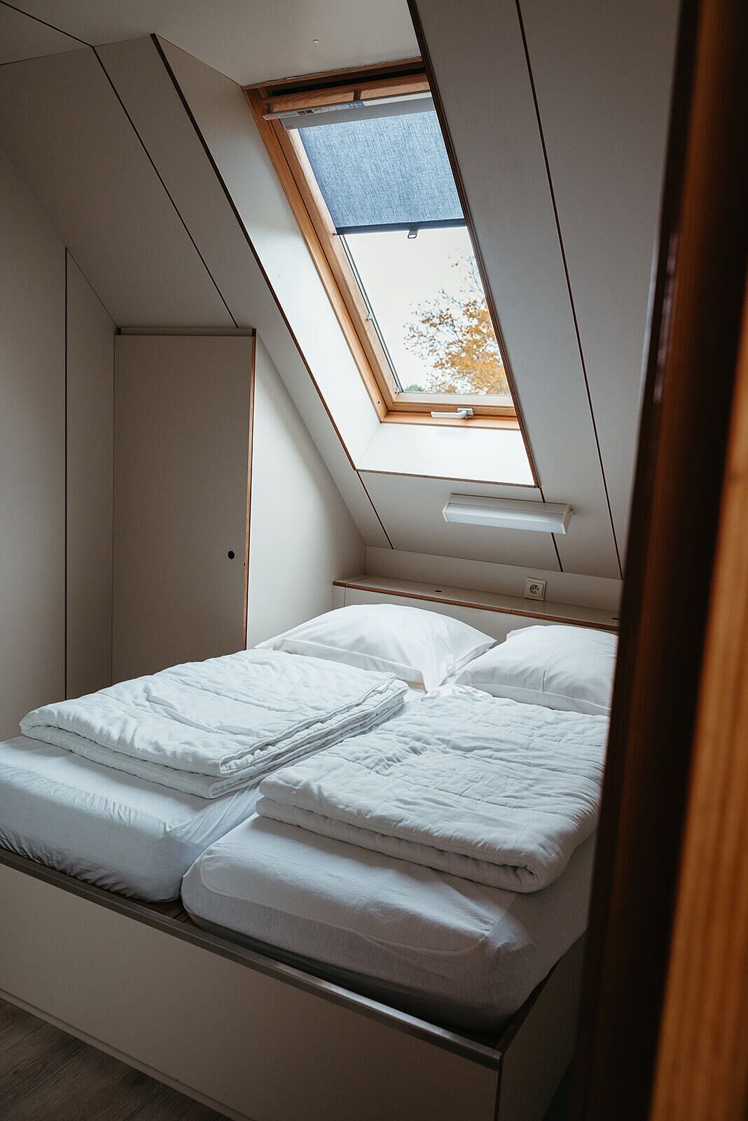 Un dormitorio pequeño con tragaluz, cama con ropa de cama blanca y un armario.
