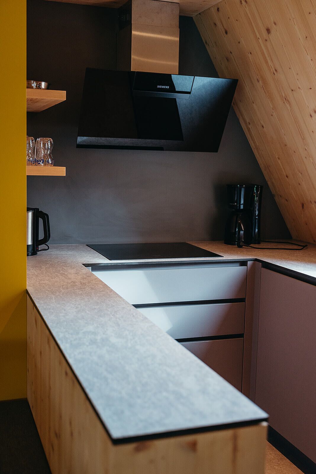 A modern kitchen with a black Siemens range hood, wooden cabinets, and a countertop with a kettle and coffee maker.