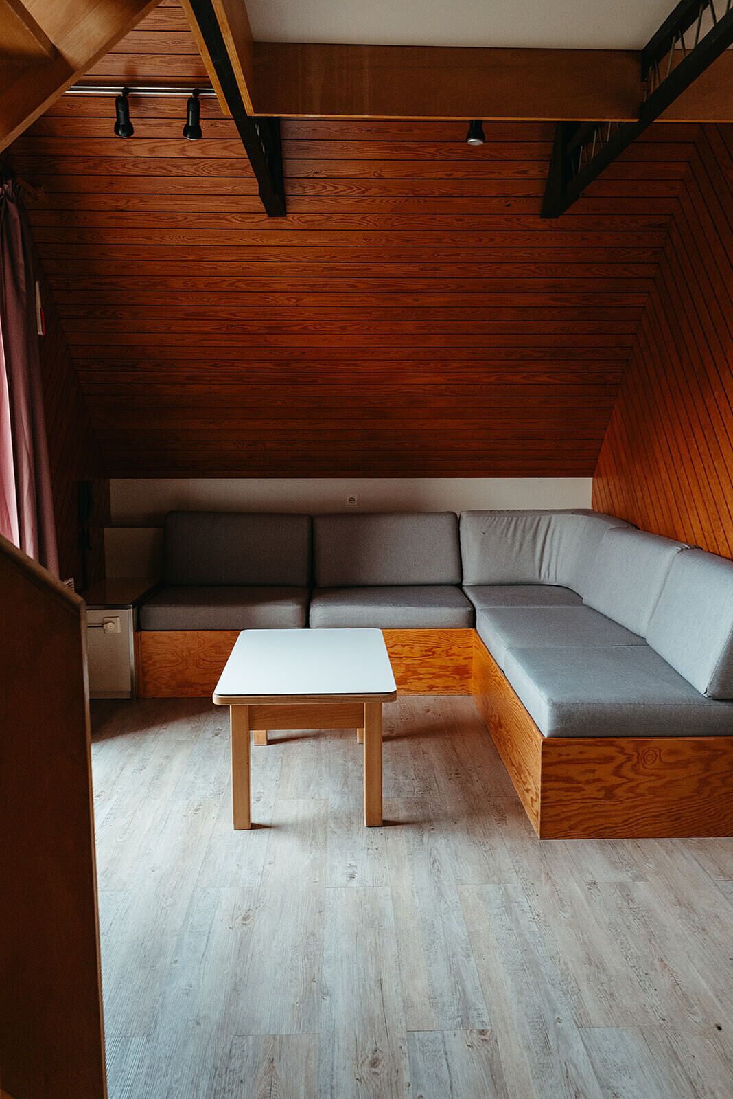 Ein gemütlicher Raum mit schrägem Dach, einer eingebauten grauen Couch und einem Holztisch.