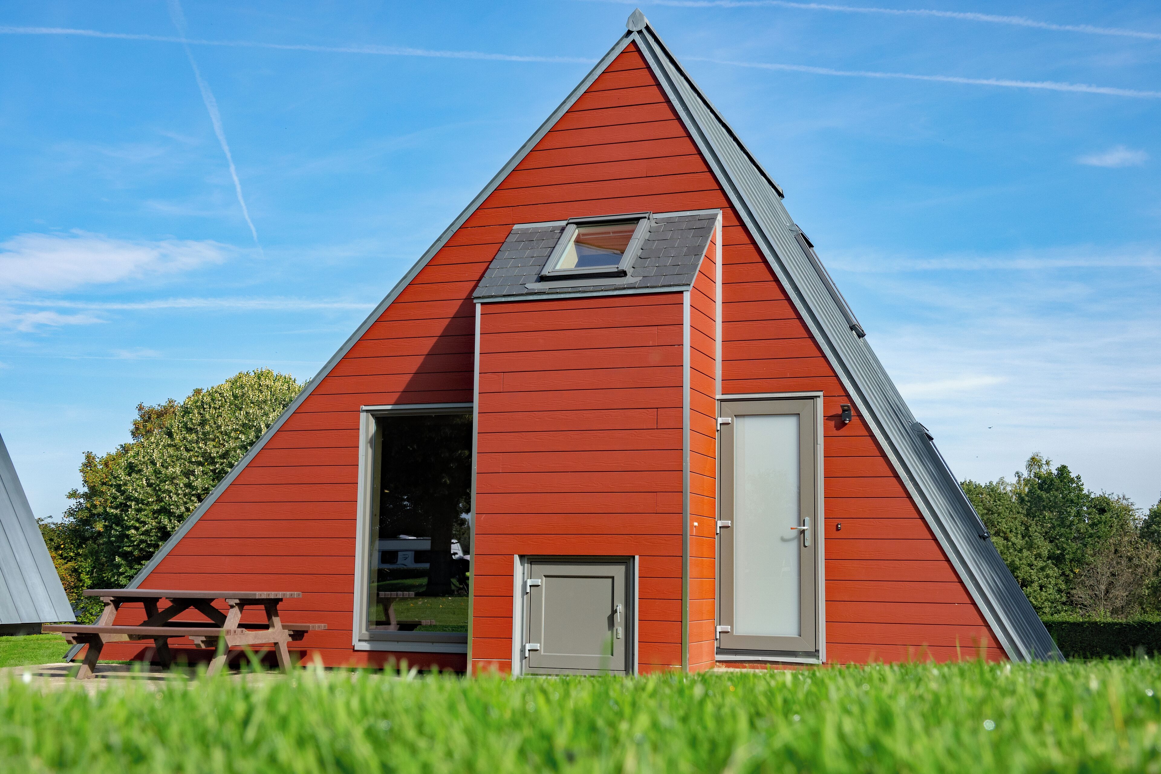 A red triangular building with a skylight and a door.