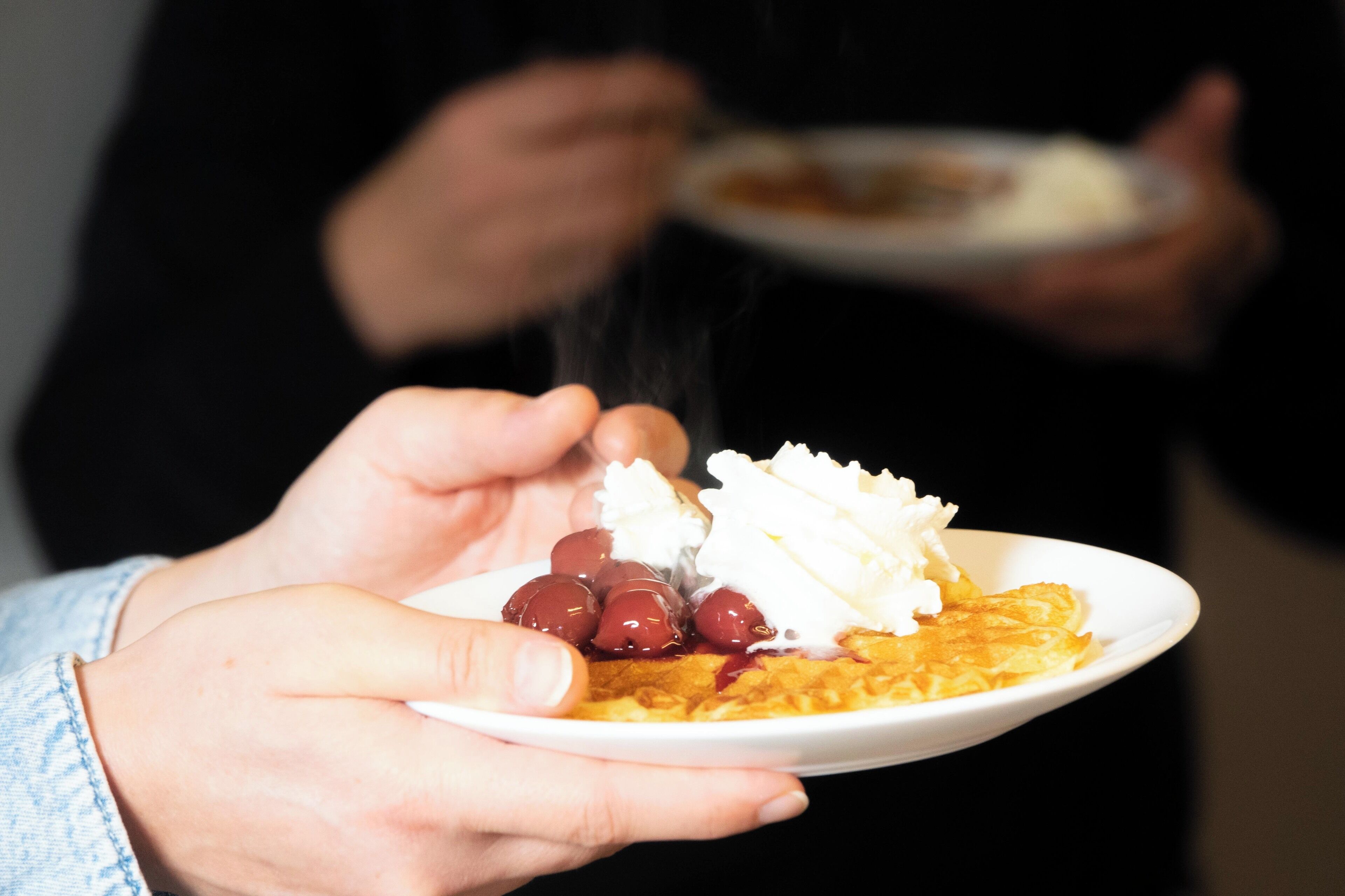 A person holding a plate with a dessert topped with whipped cream and cherries.