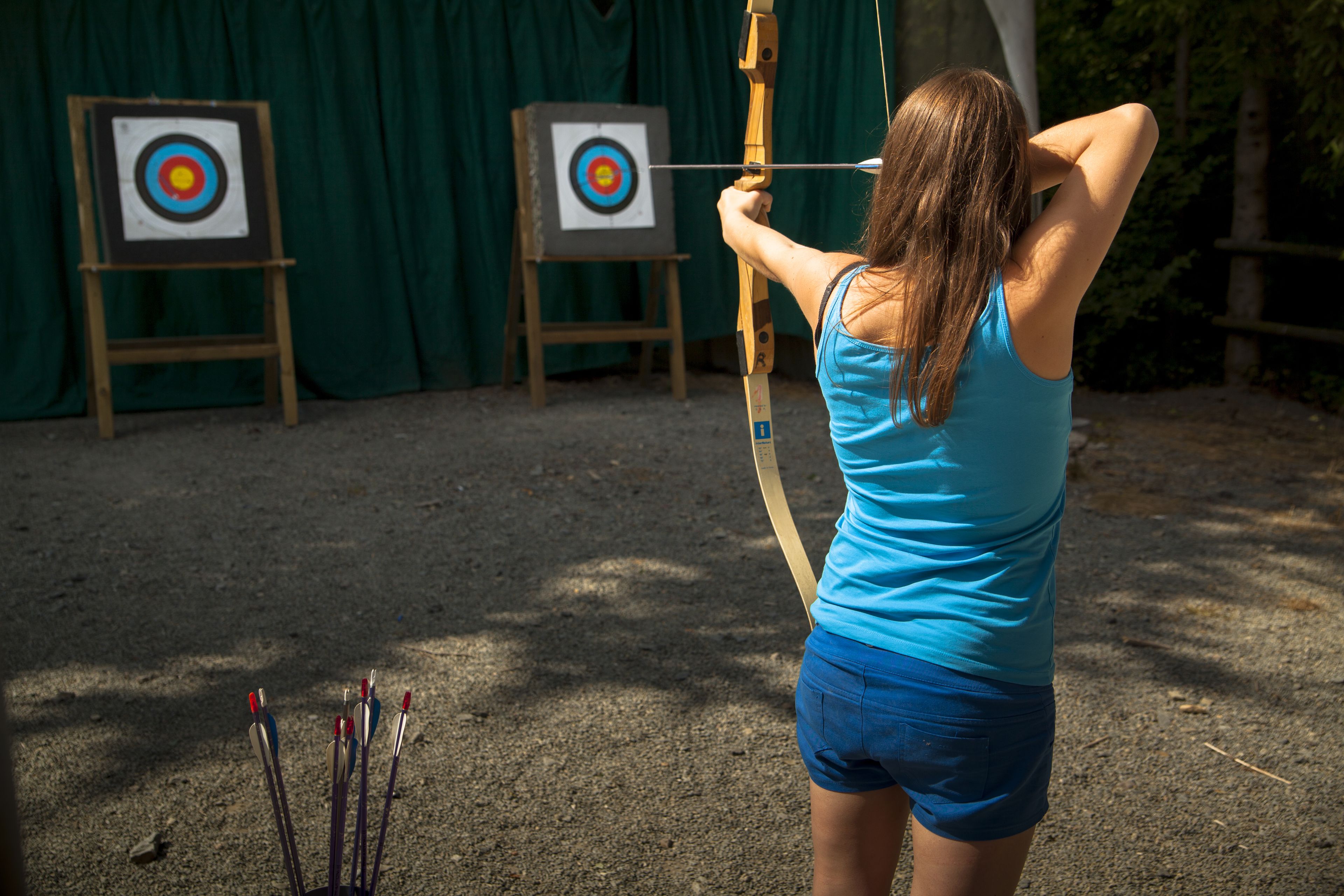 An archer aiming at a target with arrows on the ground.