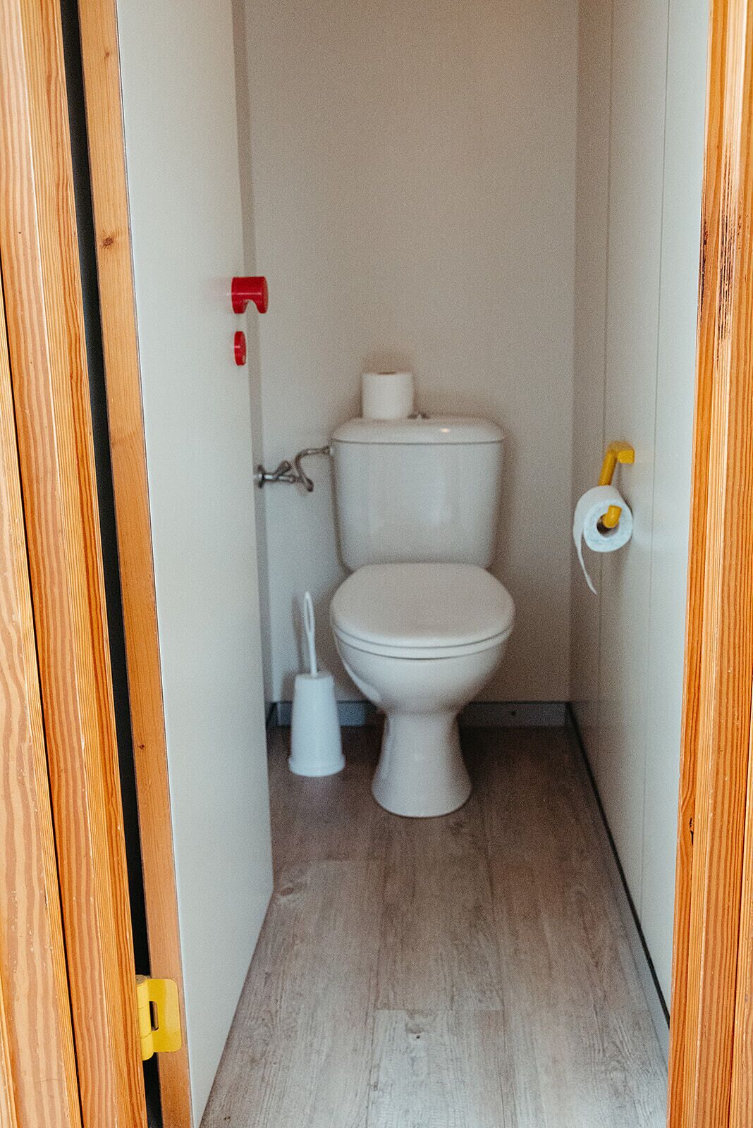 A small, narrow bathroom with a white toilet, a toilet paper holder, and a bidet.