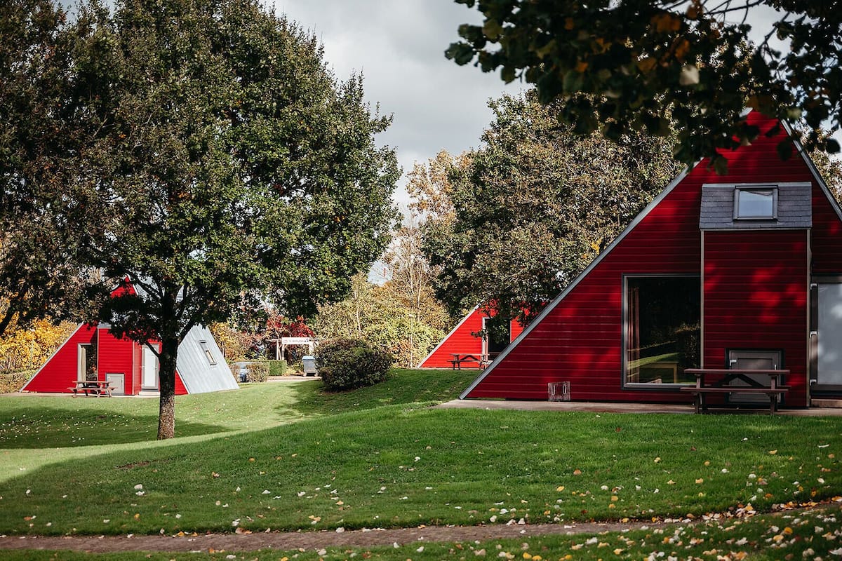 A red triangular building with a window and a door, surrounded by green grass and trees.